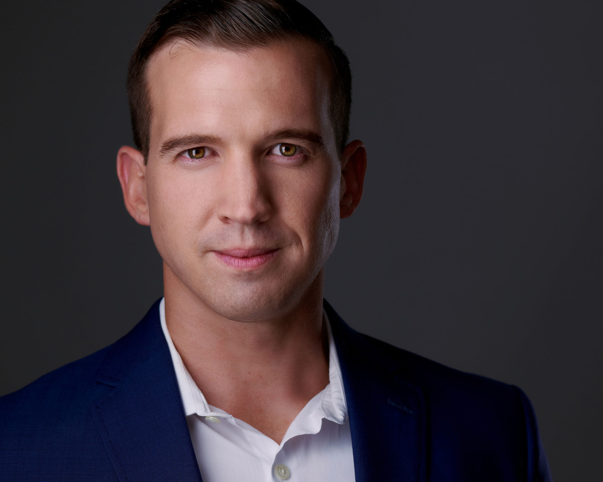 Professional man in a navy blazer photographed against a dark studio background