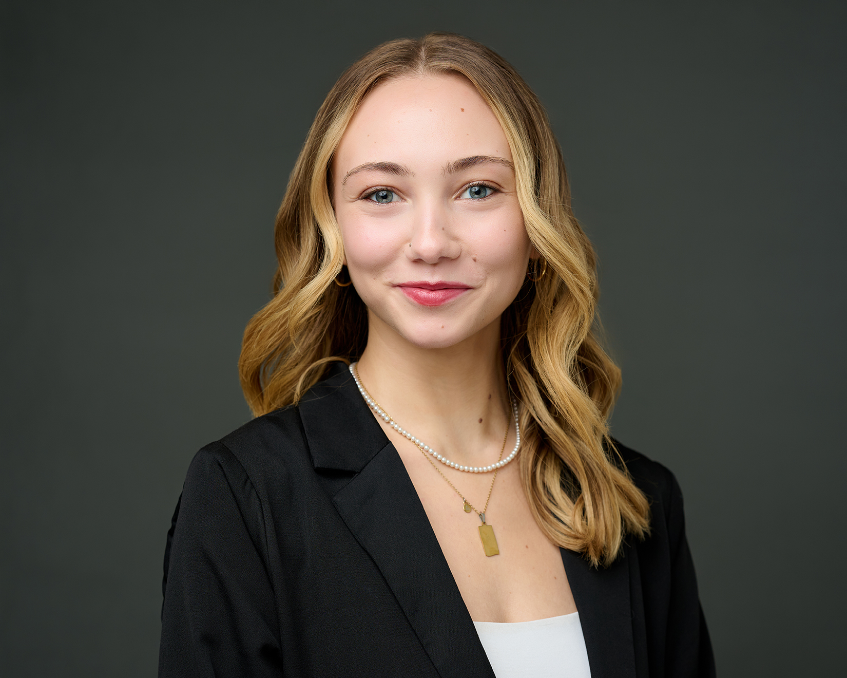 Professional woman in a black blazer and pearl necklace against a dark gray background